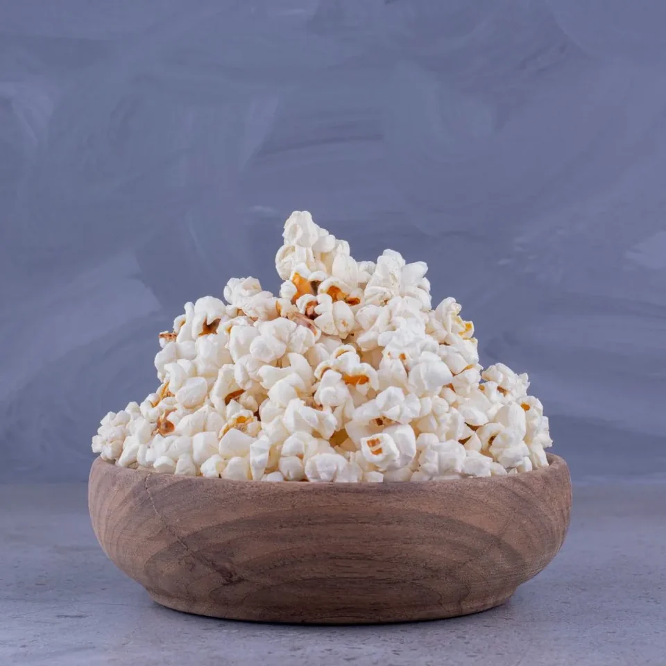 Generous serving of freshly cooked popcorn in wooden bowl on marble background high quality photo